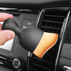 A hand holds a black silicone car interior cleaning brush with a light wood-colored bristles against a dark grille.