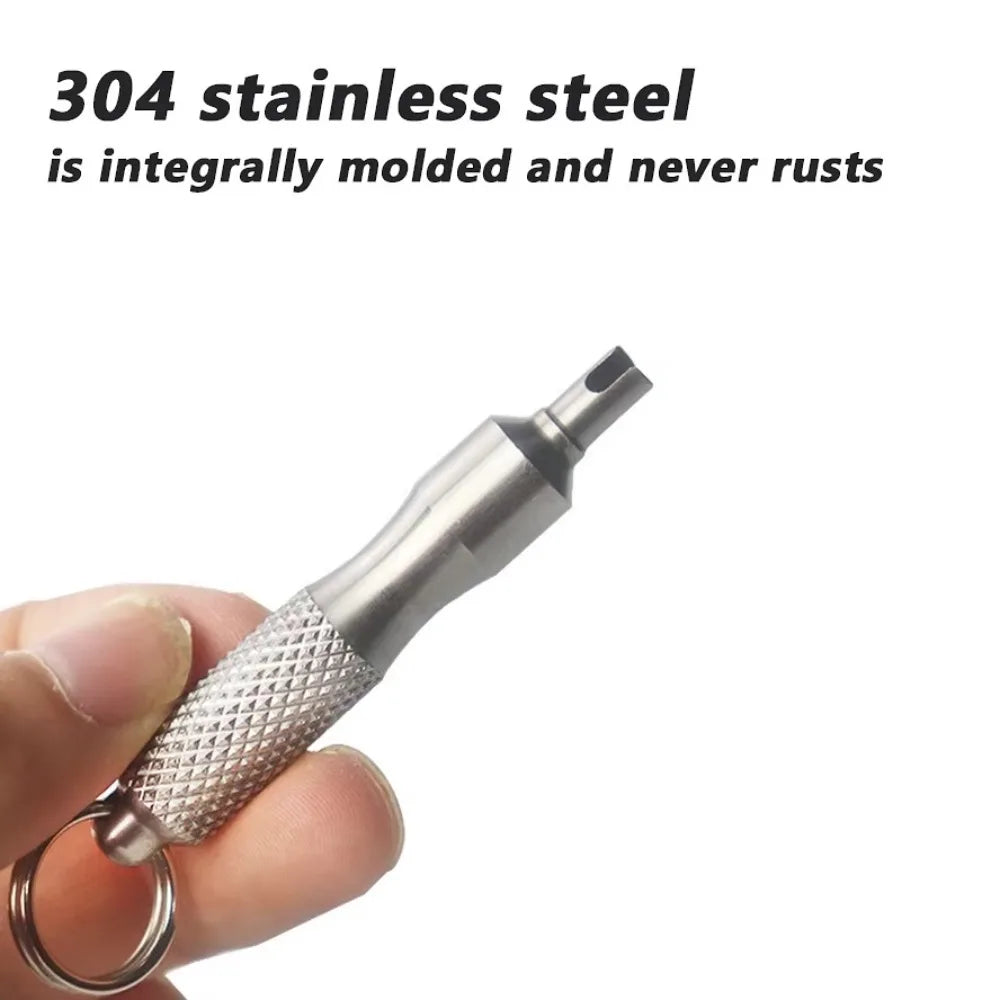 A hand is holding a stainless steel tire valve core remover tool, showing the textured tip and metal ring.