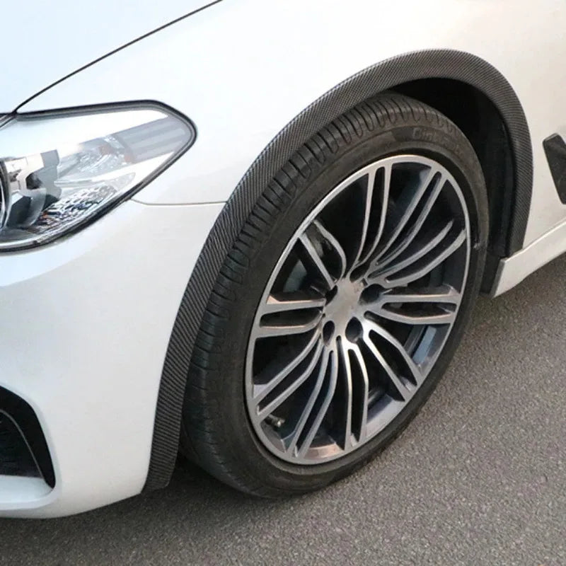 Close-up of a silver alloy car wheel with a tire and black carbon fiber trim visible on the fender.