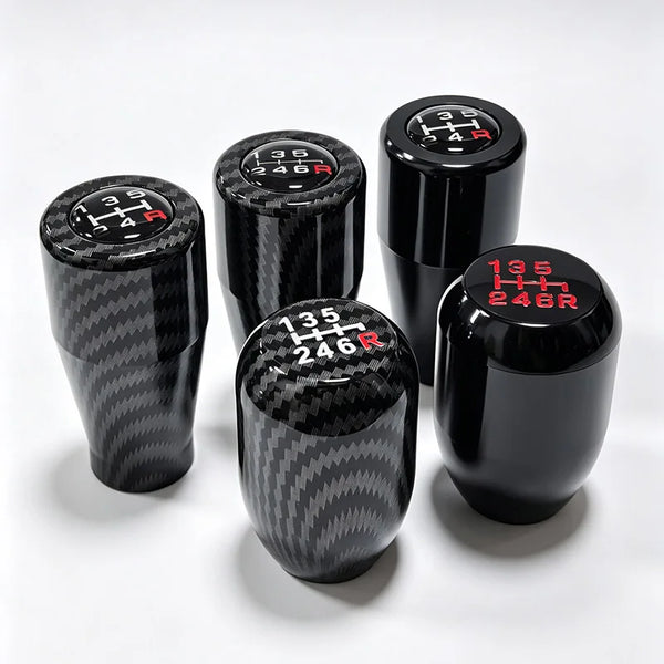 A set of black gear shift knobs with numbered markings are displayed on a white surface.