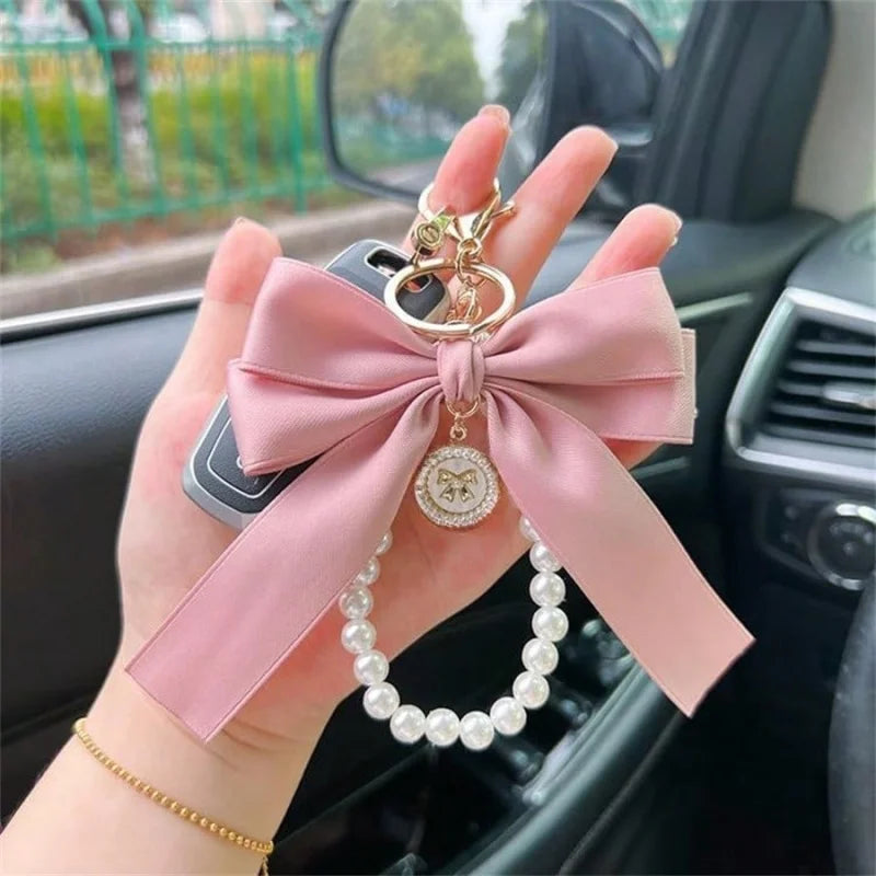 A pink ribbon lanyard with a round pearl bead pendant is held in a hand inside a car interior.