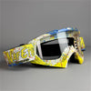 A pair of yellow and white motorcycle off-road goggles with a colorful pattern resting on a gray surface.