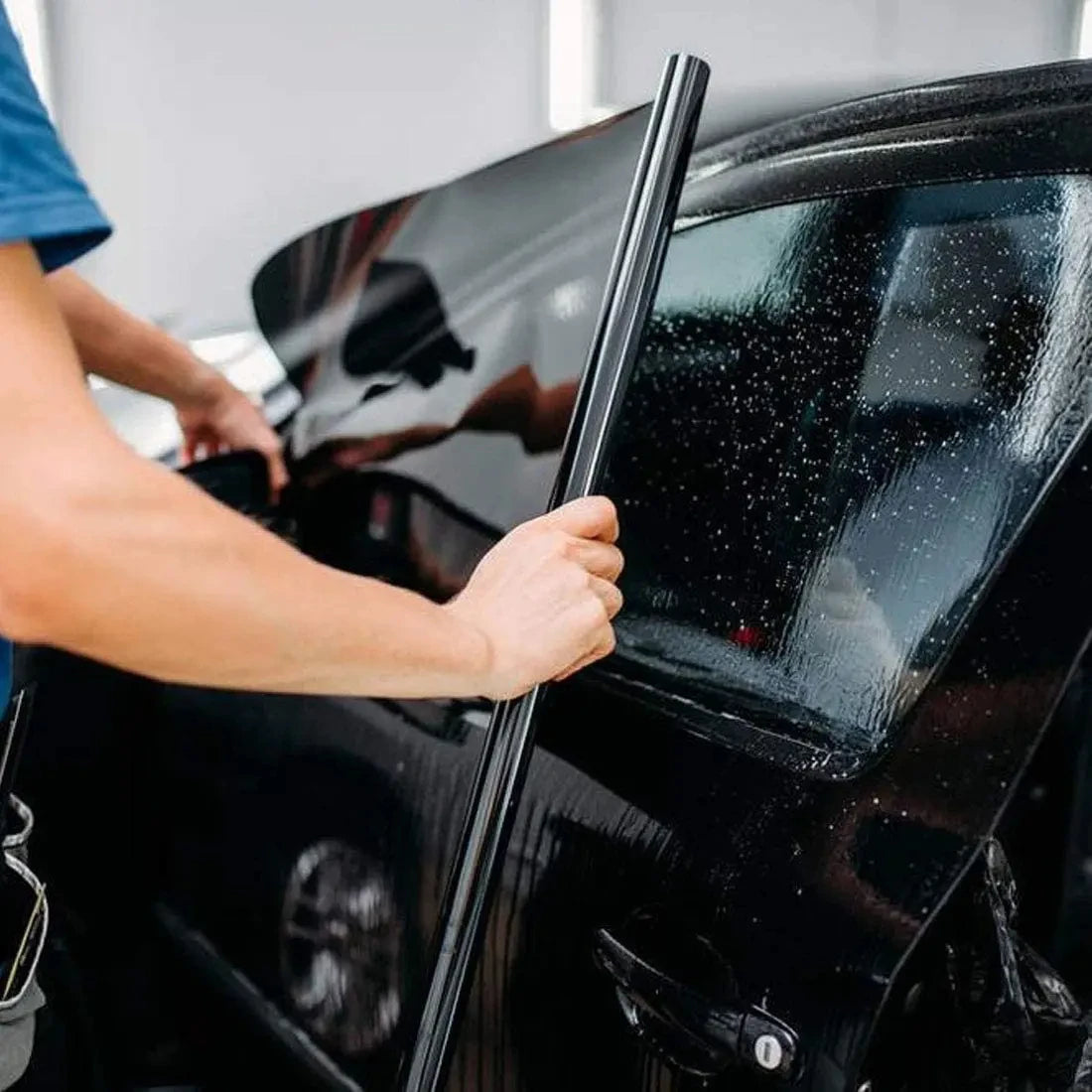 A hand is applying a car window privacy film to a dark-colored vehicle.