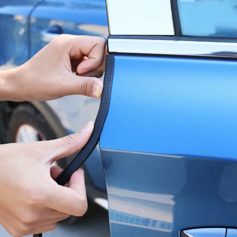 A hand is installing a black door edge protector trim on the blue body of a car door.