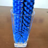 A glass filled with bright blue drill brushes for wheels and tires