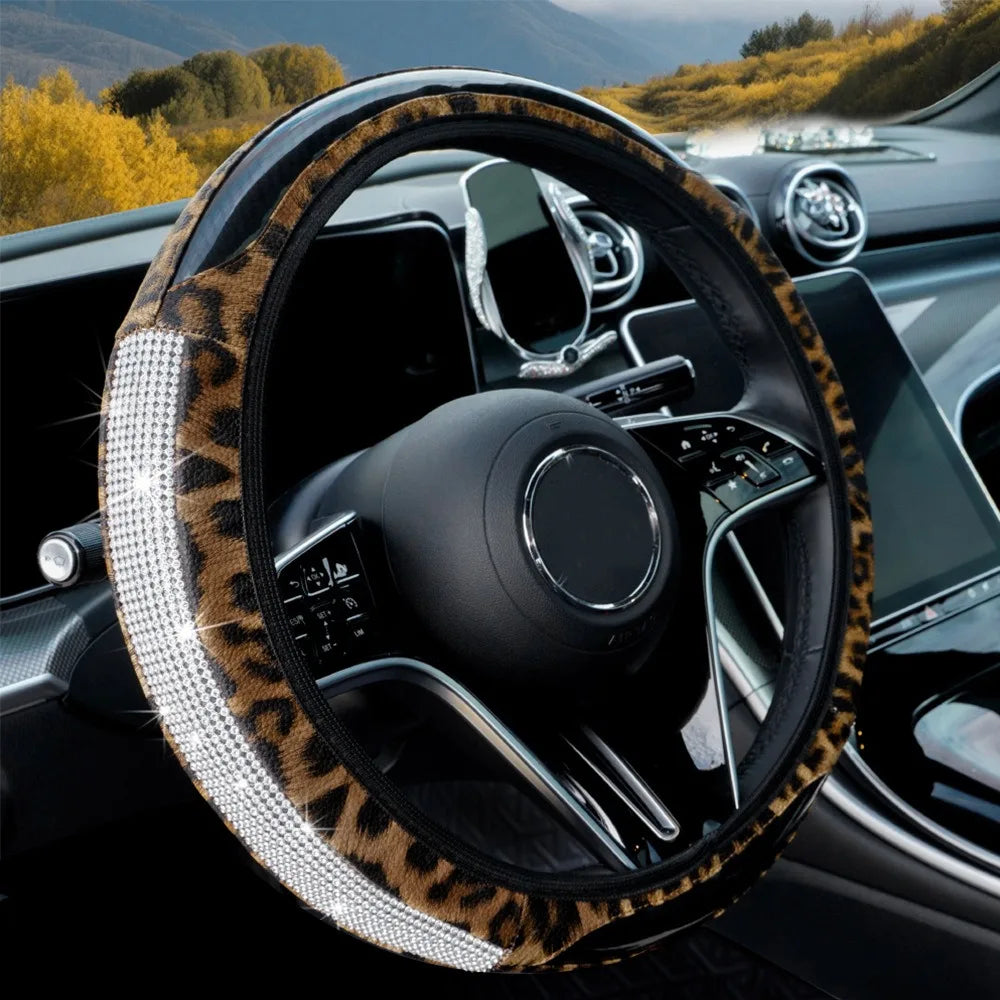 A close-up view of a black steering wheel with a leopard print cover and rhinestone accents inside a car interior.