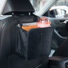 A black car trash organizer with a pink lid and an orange notebook resting in the cup holder area of a car seat.