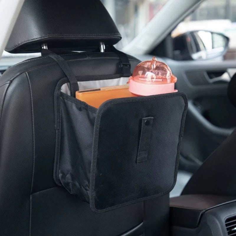 A black car trash organizer with a pink lid and an orange notebook resting in the cup holder area of a car seat.