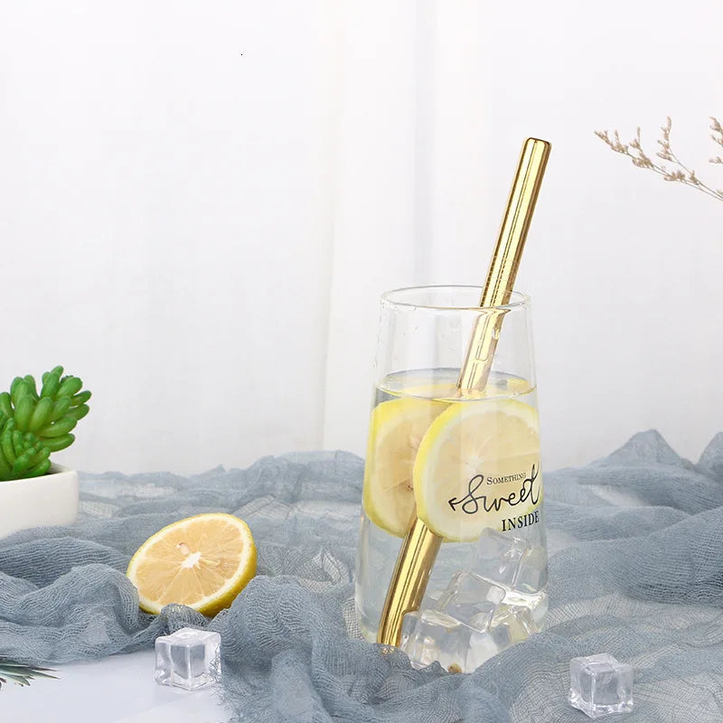 Ein Glas Zitronenwasser mit goldfarbener Trinkstroh, platziert auf grauem Stoff.