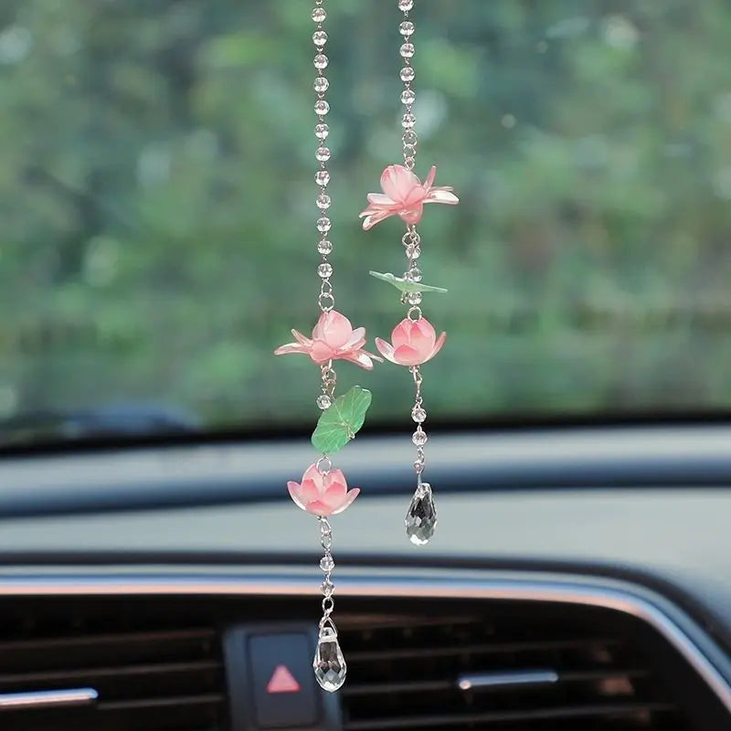 A pink lotus car pendant ornament with delicate chain and green accents hanging in a car interior.