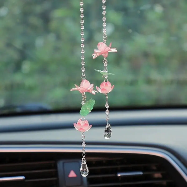 A pink lotus car pendant ornament with delicate chain and green accents hanging in a car interior.