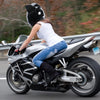 A person wearing a white shirt and jeans is riding a black motorcycle with a full face helmet in motion.