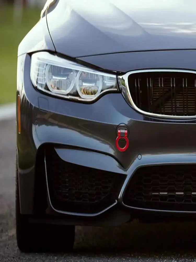 Gros plan sur le phare et la grille avant d'une voiture gris foncé avec des crochets de remorque rouges installés.