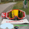 A pair of red and black motocross goggles resting on a gray surface with a white cloth underneath.