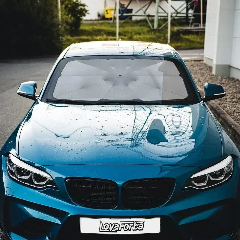 A close-up shot of a blue BMW with a black retractable car sunshade installed on the windshield.