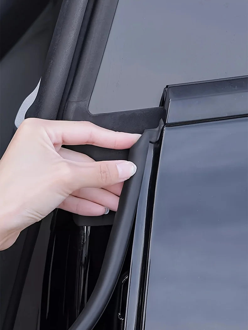 A hand is pressing a black rubber seal strip, a universal car door edge weatherstrip, into the B-pillar of a vehicle.