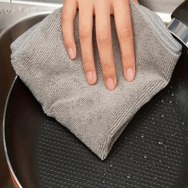 Eine Hand hält ein graues Mikrofasertuch über eine schwarze Pfanne.