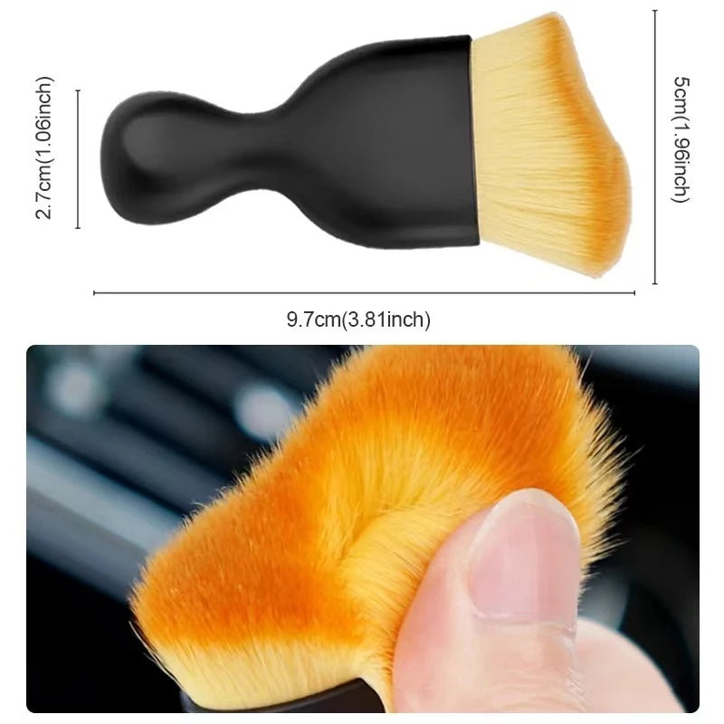 Nahaufnahme einer orangen Auto-Lüftungsreinigungsbürste mit schwarzem Griff, gehalten von einer Hand.
