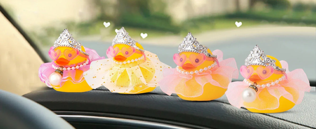 A row of decorative car rubber ducks in pink and yellow with sparkly crowns and pearl accessories resting on a car seat.