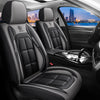Interior view of a car with black leather seat covers and steering wheel, showing the seats and a city skyline outside.