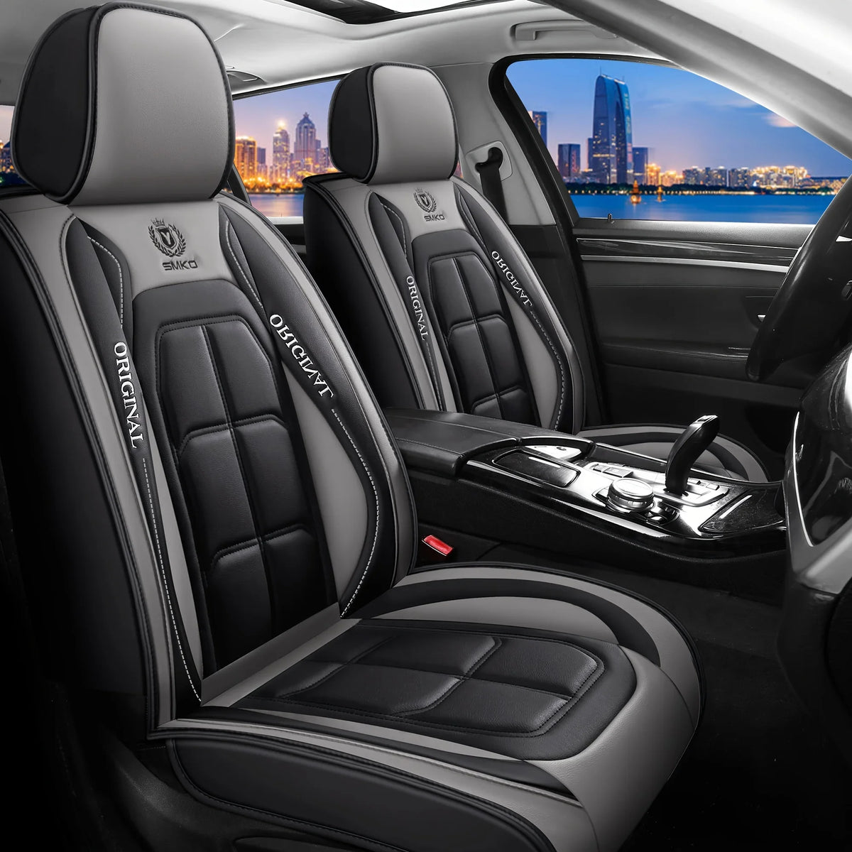 Interior view of a car with black leather seat covers and steering wheel, showing the seats and a city skyline outside.