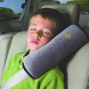A young boy is resting his head on a green car seat belt shoulder cushion inside a car seat.