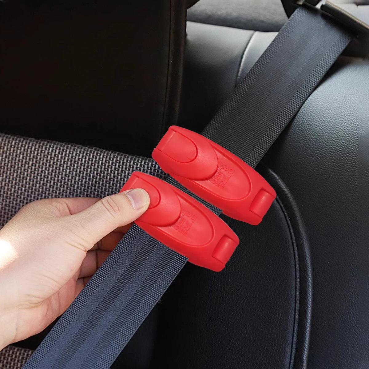 A hand is clipping a red seat belt adjuster onto a dark gray seat belt strap inside a car seat.