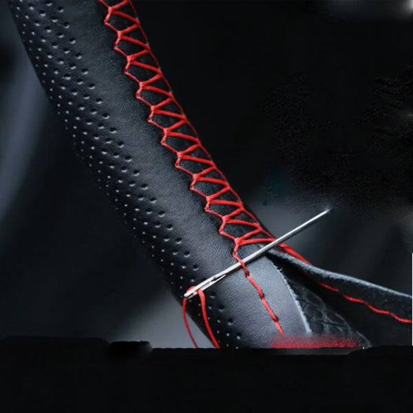Close-up of a black faux leather steering wheel cover with red stitching and a needle being used for sewing.