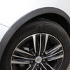 Close-up view of a black alloy car wheel with a polished rim and tire, showing carbon fiber trim on the wheel arch.