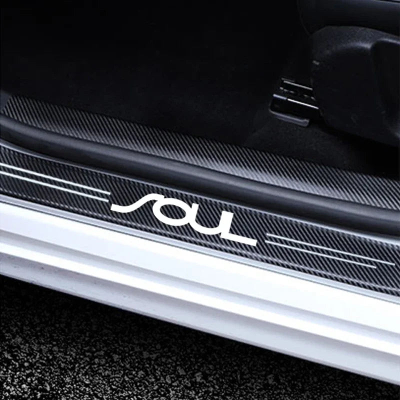 Close-up of a black carbon fiber door sill protector with a white custom logo on the side.