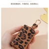 A hand holds a small leather key holder with a leopard print design and a gold-toned clasp.