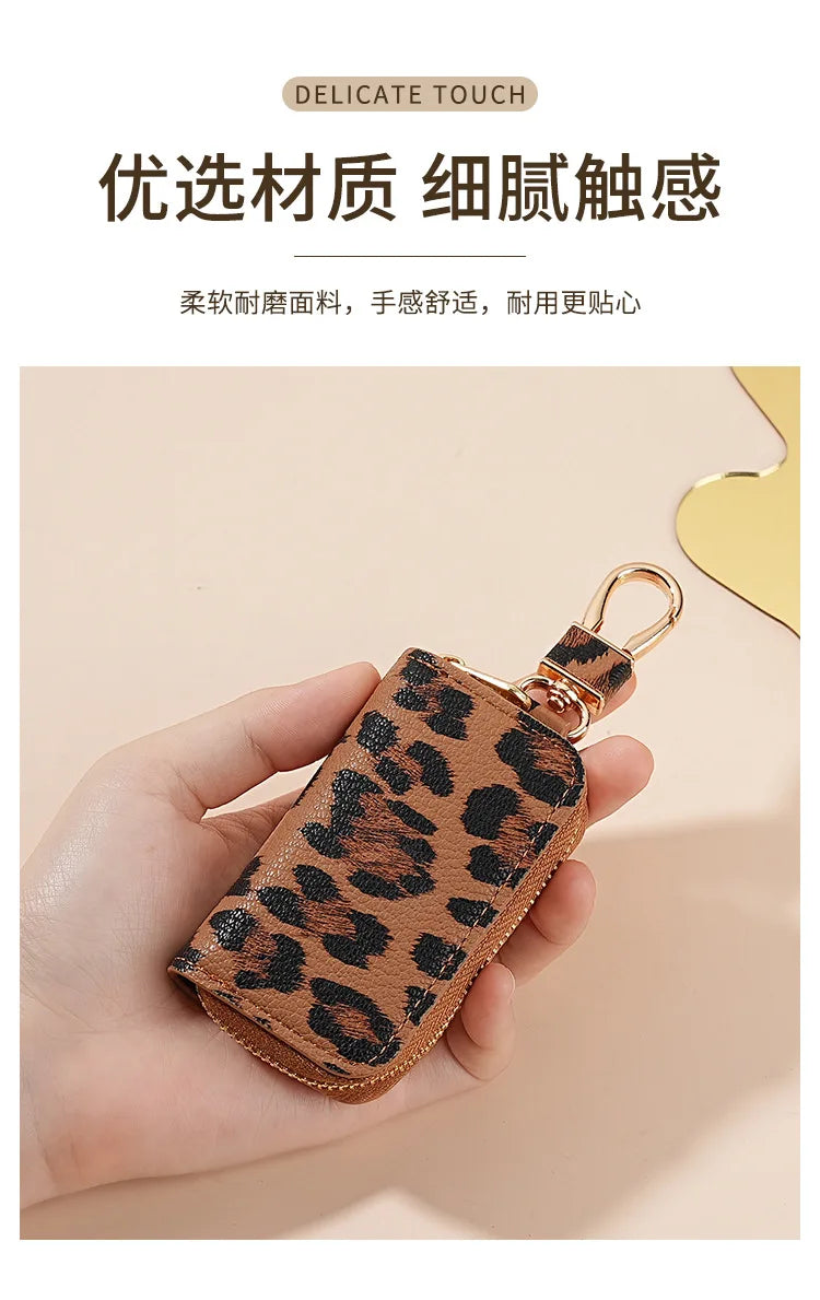 A hand holds a small leather key holder with a leopard print design and a gold-toned clasp.