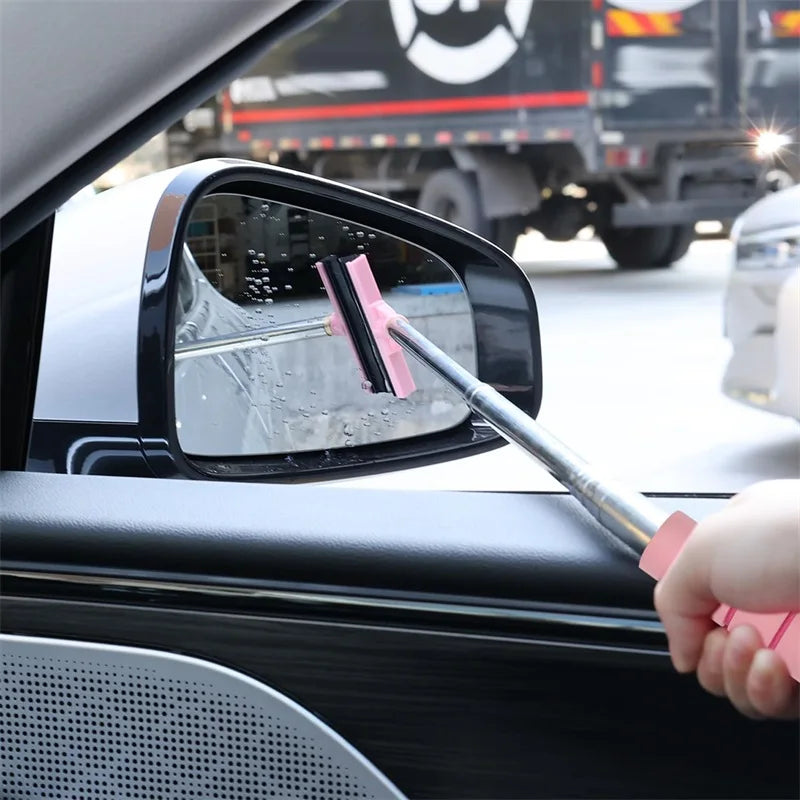A hand uses a pink glass cleaning tool to wipe the exterior of a car's side mirror.