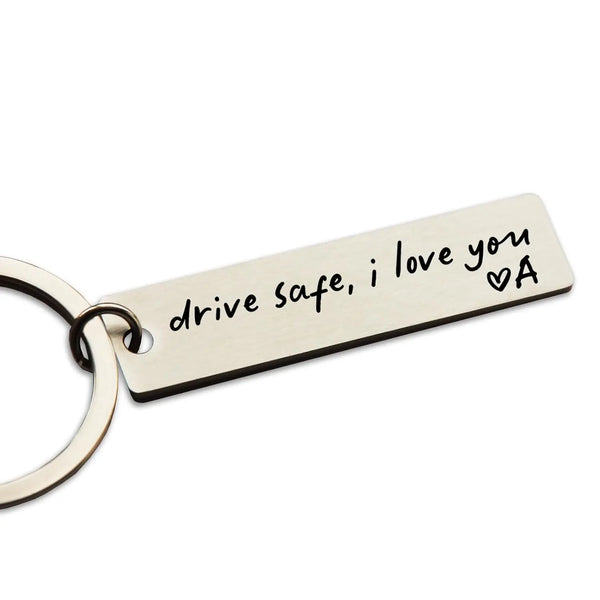A rectangular stainless steel keychain engraved with the message drive safe i love you and a heart symbol