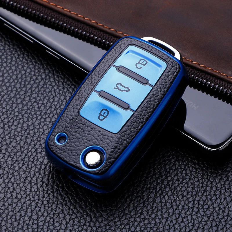 A blue TPU leather car key case with multiple buttons rests on a black leather surface.