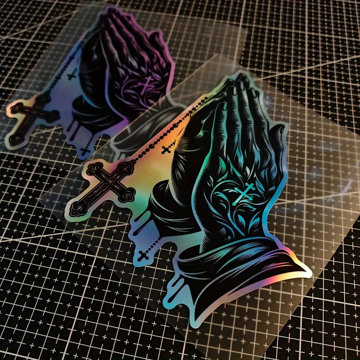 A black decal of praying hands with a cross design is shown on a transparent sheet.
