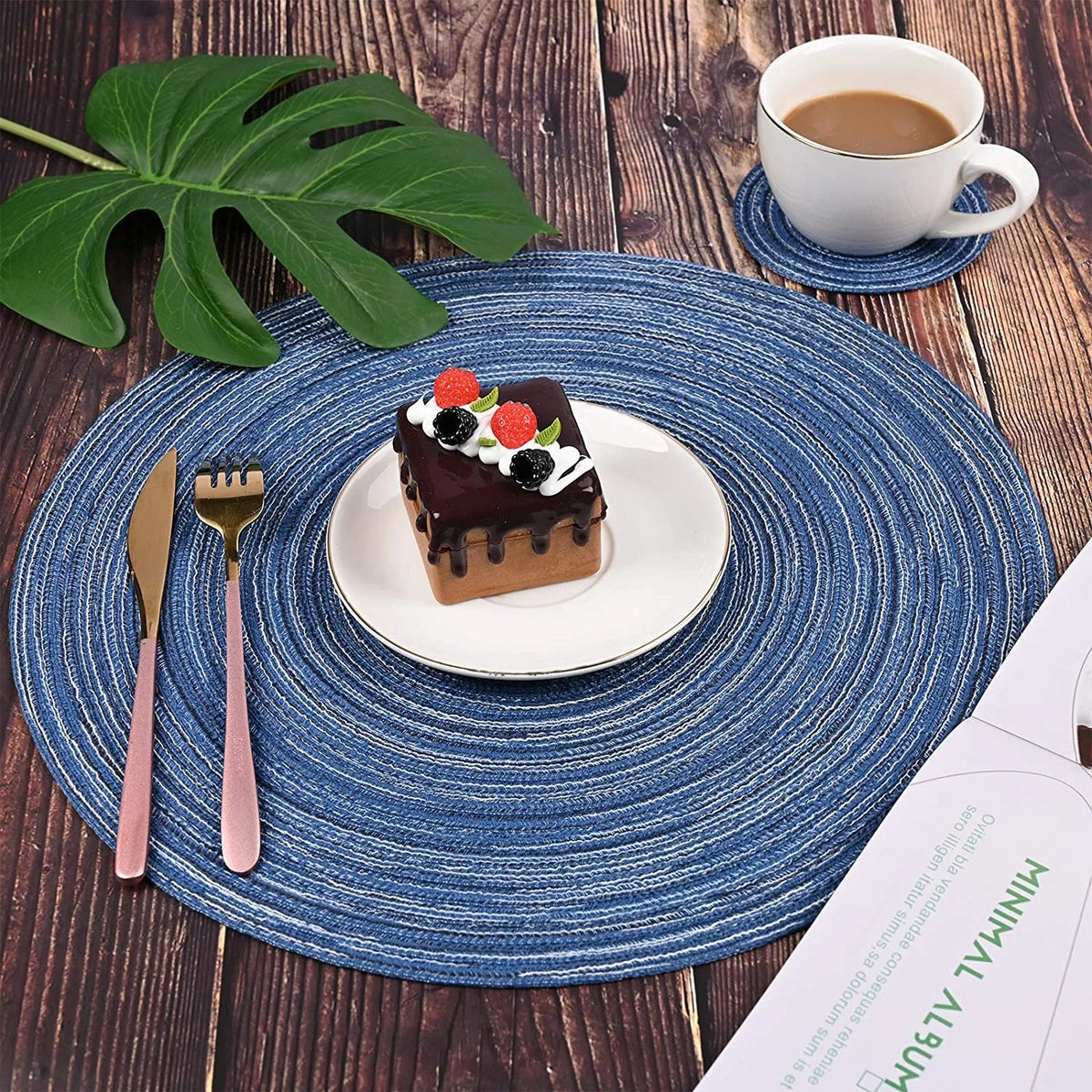 Un gâteau au chocolat garni de baies est centré sur un sous-plat en tissé bleu, à côté d'une tasse et d'un couteau.
