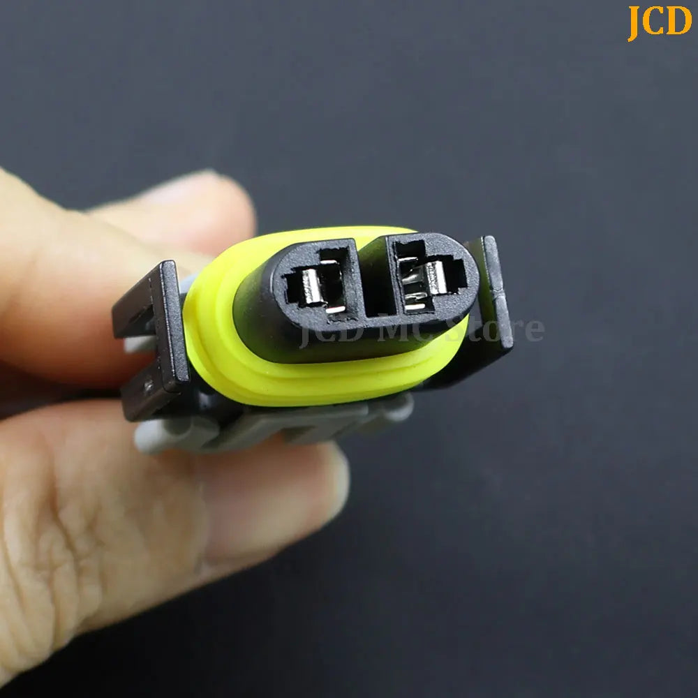 A hand holds a black HID/LED car adapter wiring harness with a yellow connector tip.
