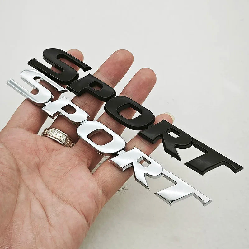 A hand holds several chrome and black 3D car logo emblems arranged in a row.