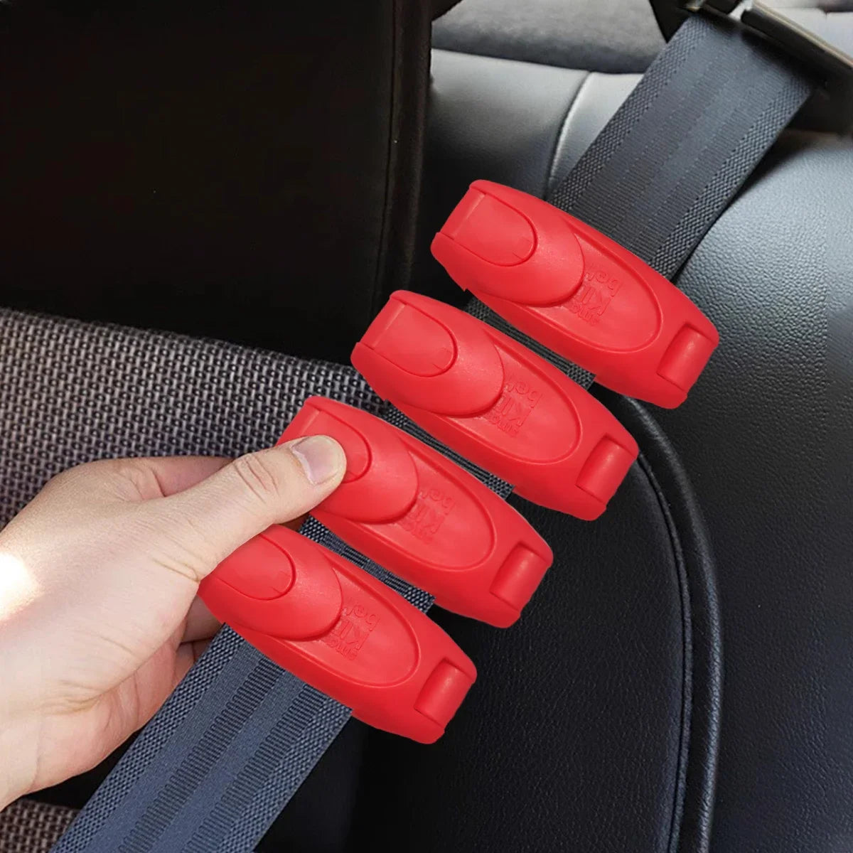 A hand is holding several red comfort-adjustable seat belt clips attached to a black car seat or upholstery.