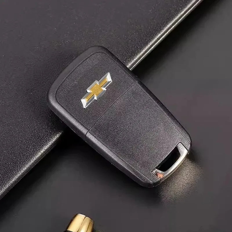 A black key fob with a gold-colored Chevrolet emblem sticker set resting on a dark surface.