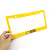 A yellow license plate frame decoration with a black Fake Taxi label is held by a hand.