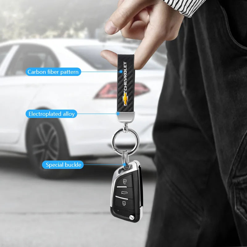 A hand holds a black key fob attached to a carbon fiber patterned keychain with an electroplated alloy and special buckle.