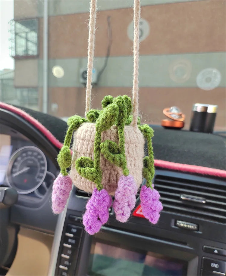 A handmade strawberry crochet hanging decoration with green vines and purple flowers displayed on a car dashboard.