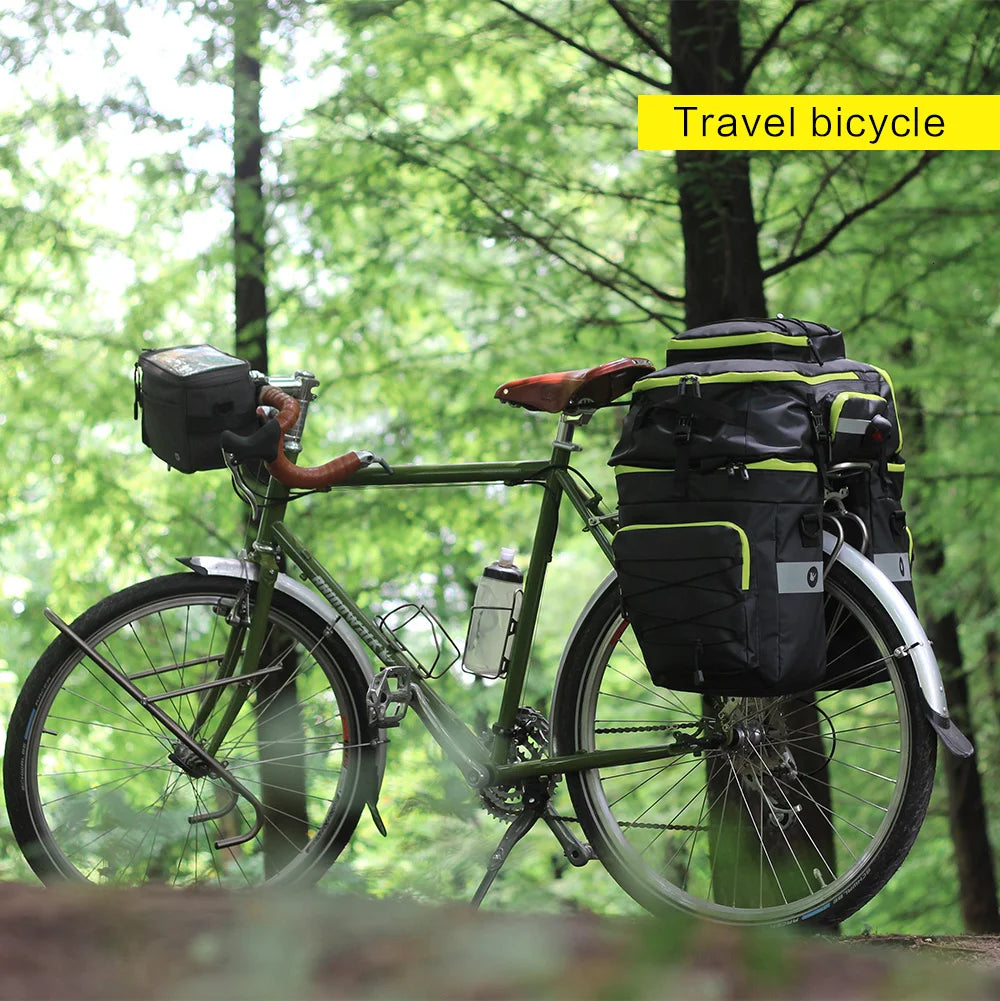 A green travel bicycle equipped with a black trunk bag and a rear rack in a wooded outdoor setting.