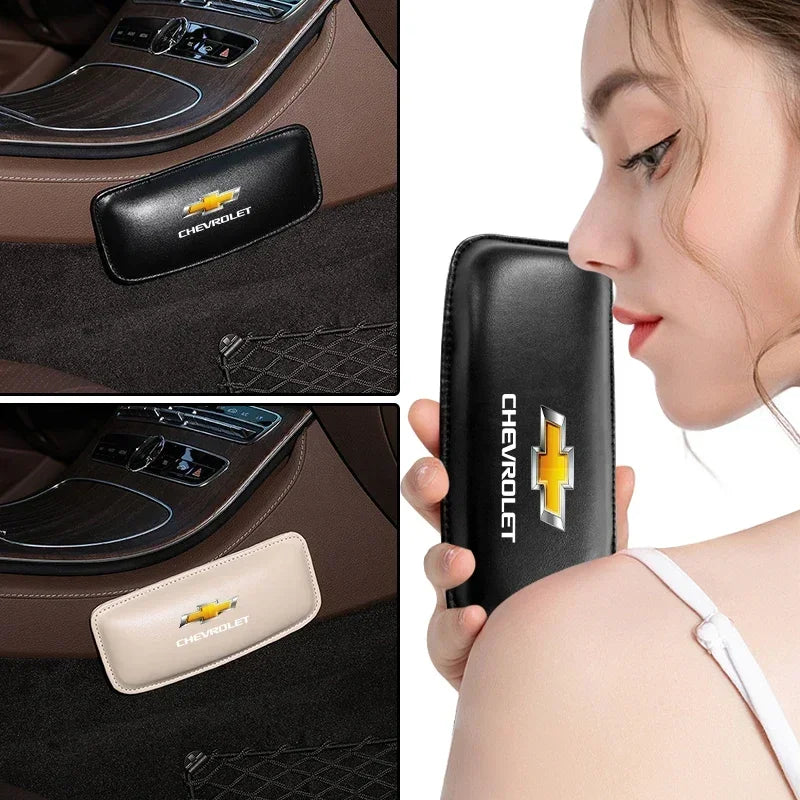 A hand holds a black leather Chevrolet keychain and a silver leather knee pad for car driving.