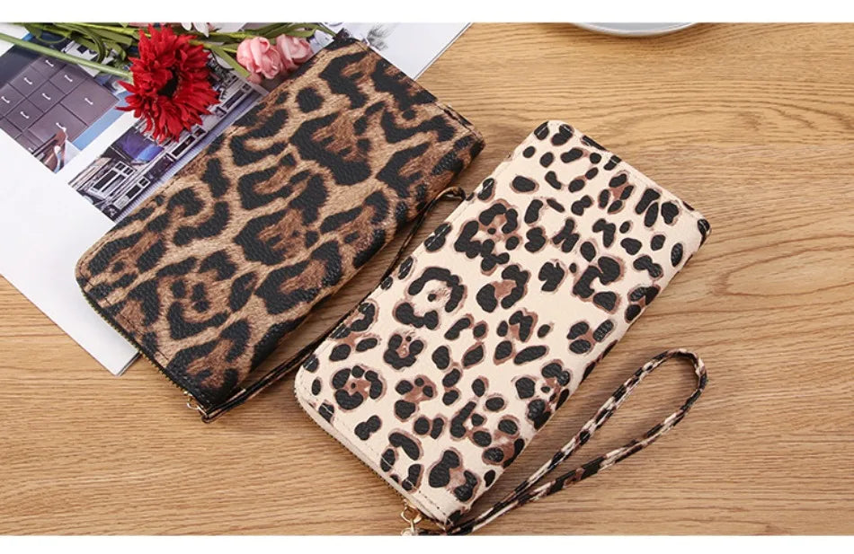 A pair of leopard print long wallets, one dark brown and one beige, resting on a wooden surface.