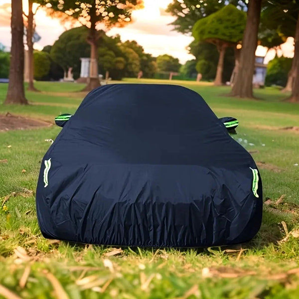 A dark blue universal all-weather car cover is laid out on green grass in a park setting.