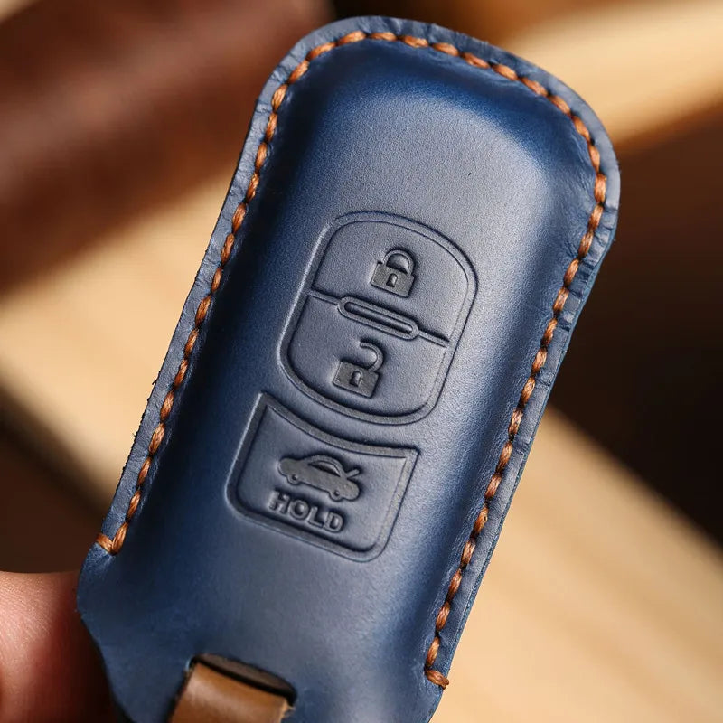 A close-up of a blue leather car key fob cover with embossed lock and hold symbols.