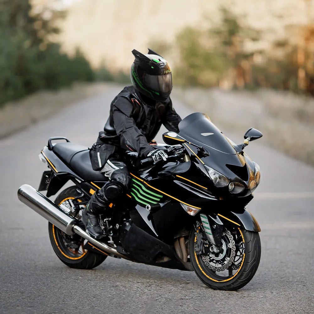 A black full face motorcycle helmet is shown parked on an asphalt road with a blurred forest background.